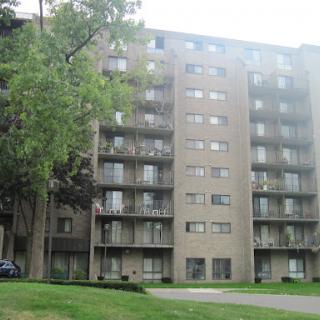 A multistory apartment building featuring balconies and surrounded by greenery.