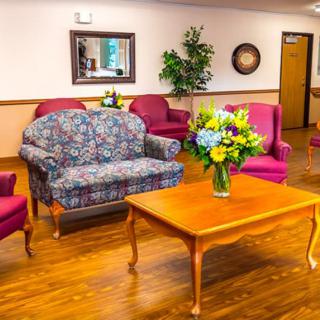 A cozy living room setup with a floral patterned sofa, red chairs, and a wooden table adorned with a vase of flowers.