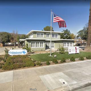 A green building with an American flag in front, surrounded by a landscaped area.