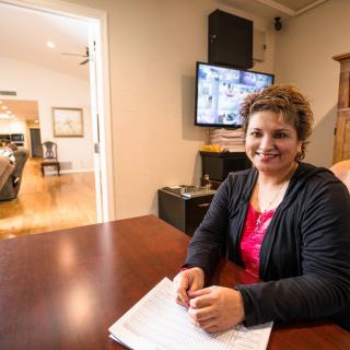 A woman sitting at a desk in an office, smiling with paperwork in front of her.