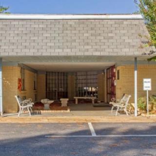 A building with a shaded entrance featuring outdoor seating and a small parking area.