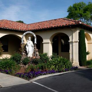A Mediterranean-style building with an arched entrance and a garden featuring a statue.