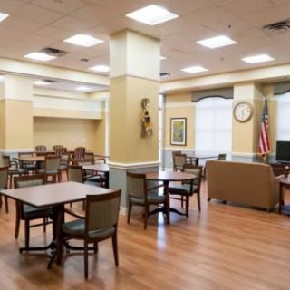A spacious and well-lit community dining area with tables and chairs arranged neatly on a wooden floor.