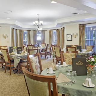 A well-set dining room with neatly arranged tables and chairs, elegant chandeliers, and large windows with curtains.