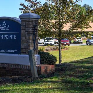 A community center sign stands at the entrance, with a building and parked cars in the background surrounded by trees.