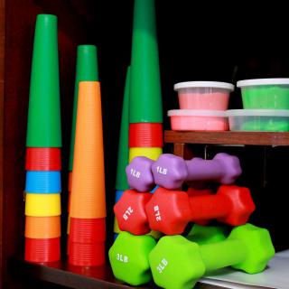 A shelf organized with colorful cones, dumbbells, and containers of play dough.