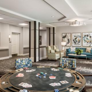 A stylish lounge featuring a poker table with cards and chips, surrounded by comfortable seating and adorned with modern artwork.