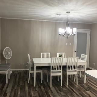 A cozy dining room featuring a white table and chairs, complemented by a stylish chandelier and modern wooden flooring.
