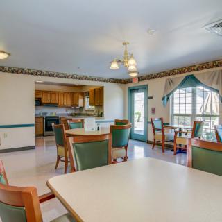 A well-lit dining area with tables and chairs adjacent to a kitchen.
