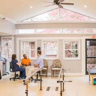 A well-lit physical therapy room with exercise equipment and people engaging in rehabilitation activities.