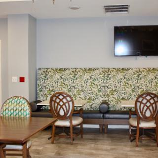 A modern living space featuring a dining table, upholstered chairs, and a decorative wall behind a television.