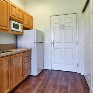 A small kitchen featuring wooden cabinets, a refrigerator, a microwave, and wood flooring.