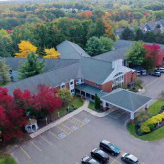 Aerial view of a suburban building surrounded by vibrant autumn foliage and a parking lot.