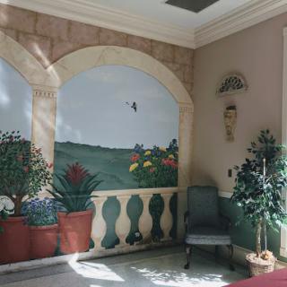 A beautifully decorated interior space featuring a mural of a landscape, potted plants, and elegant furnishings.