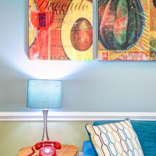 A vibrant and stylish living room featuring colorful artwork, a cozy couch, and a retro lamp.