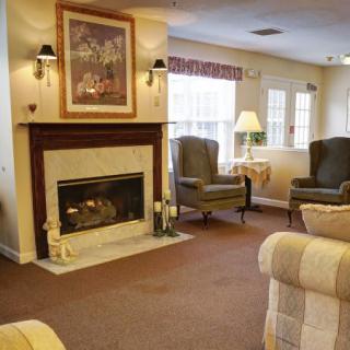 A cozy living room features a fireplace, armchairs, and natural light through the windows.