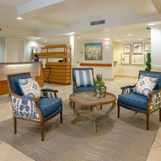 A cozy lobby area featuring blue upholstered armchairs, a round wooden table, and decorative pillows on a neutral-toned carpet.