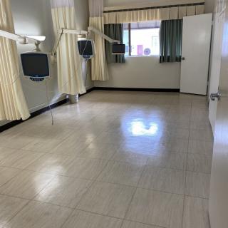 An empty hospital room with clean floors and curtains, featuring televisions by the beds.