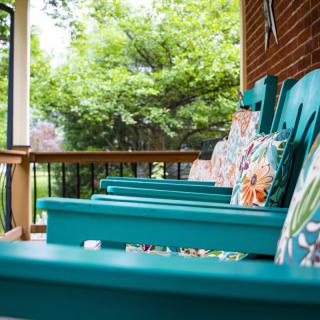 A cozy porch with turquoise chairs adorned with colorful cushions, offering a relaxing view of the surrounding greenery.