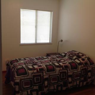 A minimalist bedroom with a single bed, patterned bedding, and a small lamp next to the window.