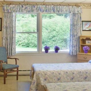 A cozy bedroom with floral curtains, a window view of greenery, and neatly arranged furniture.