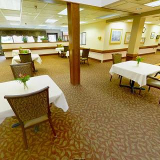 A spacious dining area with neatly arranged tables and chairs, featuring plants on each table and art on the walls.