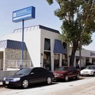 A view of a commercial building with parked cars in front and trees lining the street.