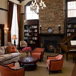 A cozy living room with a fireplace, bookshelves, and a grand piano.