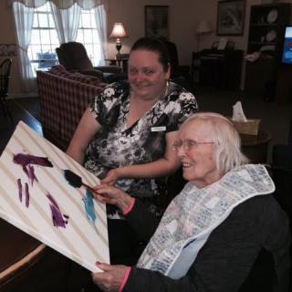 An elderly woman and her caregiver enjoy painting together.