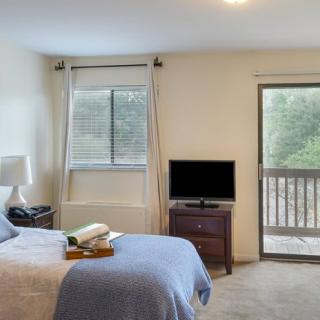 A cozy bedroom with a bed, television, window, and balcony access.