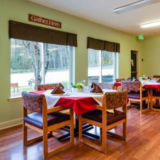 A cozy dining area with tables and chairs, set beside large windows with outside views.