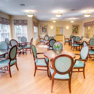 A well-lit dining area with multiple tables and chairs arranged on a wooden floor.