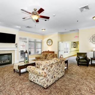 A cozy living room with a fireplace, sofa, armchairs, and a ceiling fan.