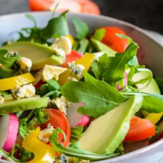 A vibrant and fresh salad with avocado, arugula, bell peppers, and tomatoes.