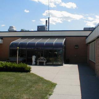 A brick building featuring a small greenhouse extension with a bench outside under a clear blue sky.