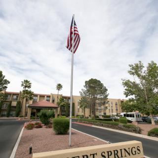 A building with a flagpole displaying the American flag set against a cloudy sky and surrounded by desert landscaping.