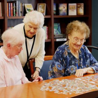 Three elderly women engaging in a puzzle activity in a library setting.