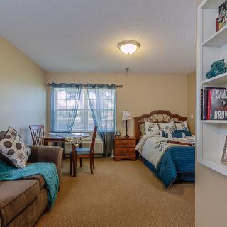 A cozy bedroom with a bed, sofa, and table near the window.