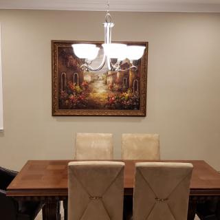 A dining room with a wooden table, four beige chairs, and a painting on the wall.