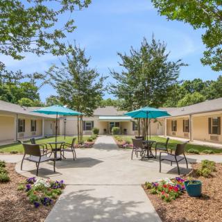 A serene courtyard with outdoor seating, featuring tables and chairs under umbrellas, surrounded by landscaped greenery.