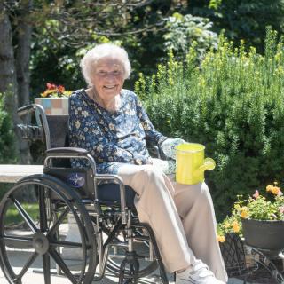 An elderly person sitting in a wheelchair, enjoying a sunny day in the garden.