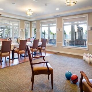 A spacious dining and activity room featuring set tables, chairs, and a corner with bowling pins and balls.