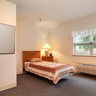 A minimalist bedroom with a single bed, lamp, and window.