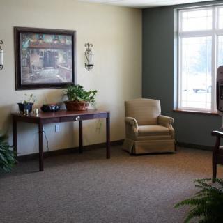 A cozy living room with a comfortable chair and table, decorated with plants and artwork.