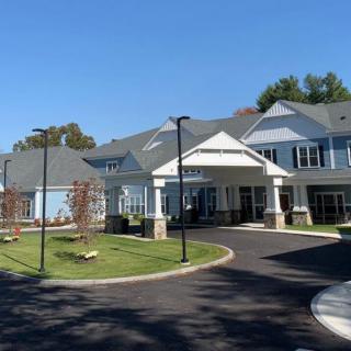 A modern residential building with a circular driveway and landscaped surroundings under a clear blue sky.