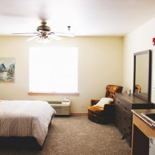 A cozy bedroom with a bed, chair, dresser, and ceiling fan.