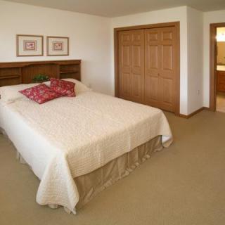 A cozy bedroom with a neatly made bed, wooden closet doors, and framed artwork on the wall.