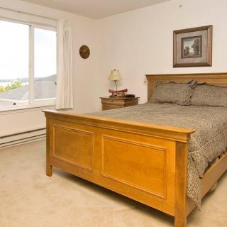 A cozy bedroom with a wooden bed frame, a nightstand with a lamp, and a window allowing natural light.