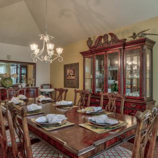 A traditional dining room with a wooden table set for a meal, surrounded by elegant chairs and illuminated by a chandelier.