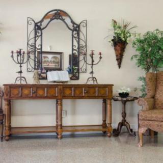 A traditional style interior setup with a wooden console table, decorative mirror, candlesticks, and various plants.